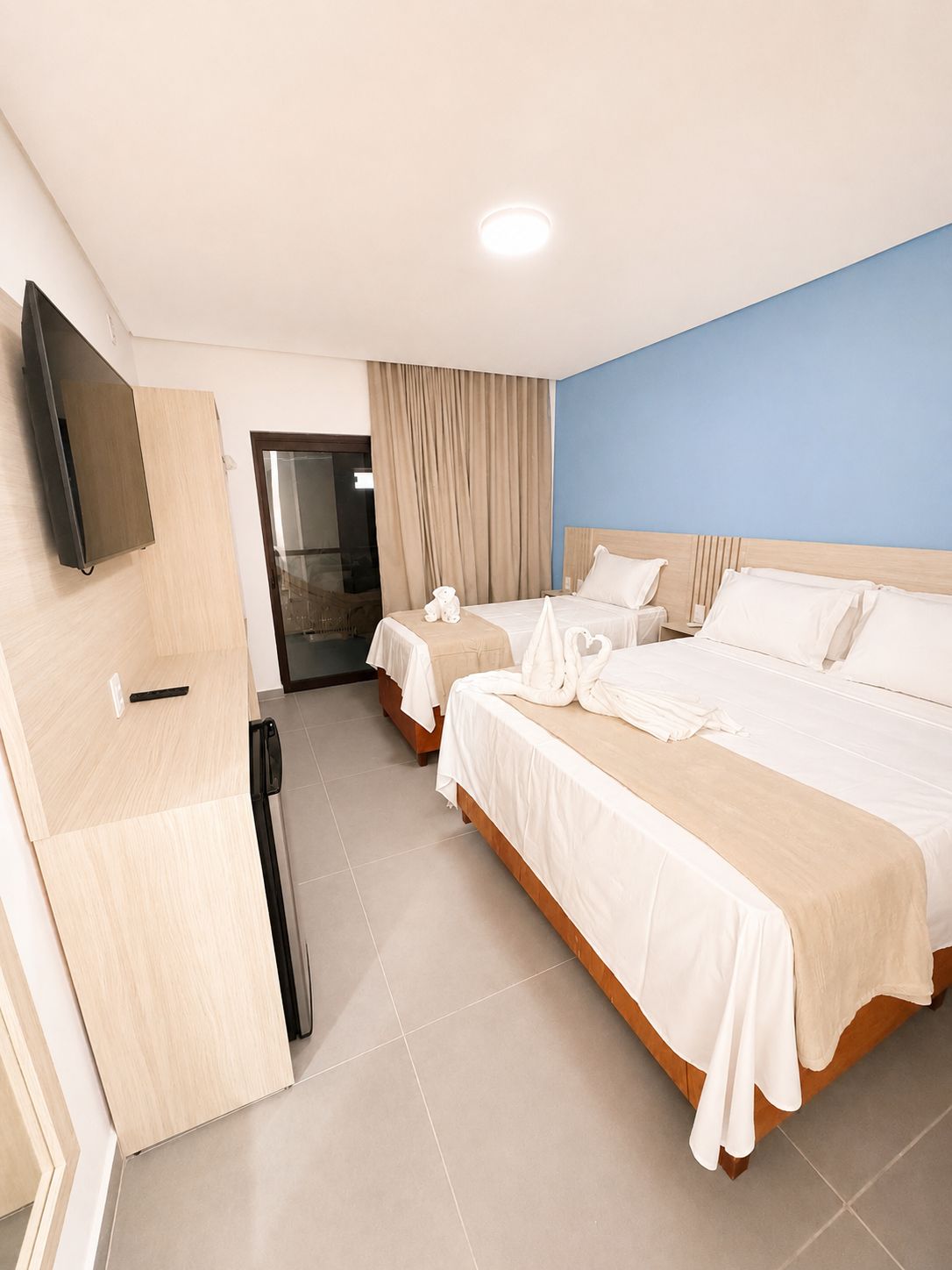 A hotel room with two beds, a flat-screen TV mounted on the wall, and a sliding door leading to a bathroom.