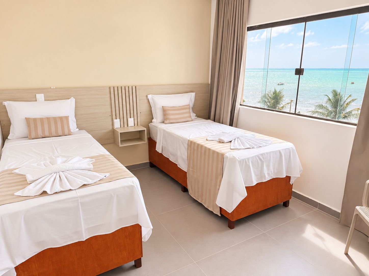 Habitación de hotel con dos camas, vista al océano y una ventana con cortinas.