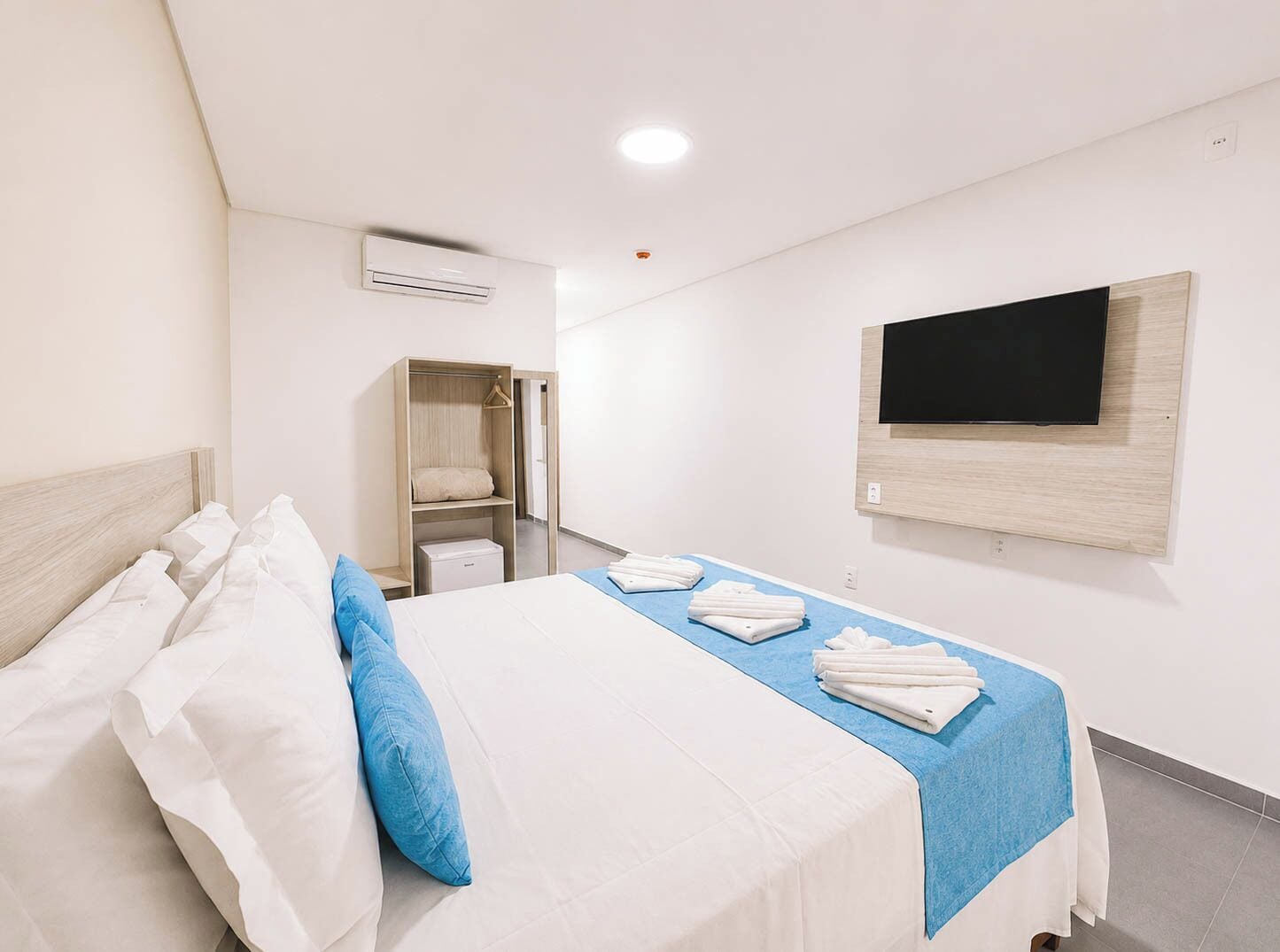 Una habitación de hotel con cama, armario, televisor y aire acondicionado.