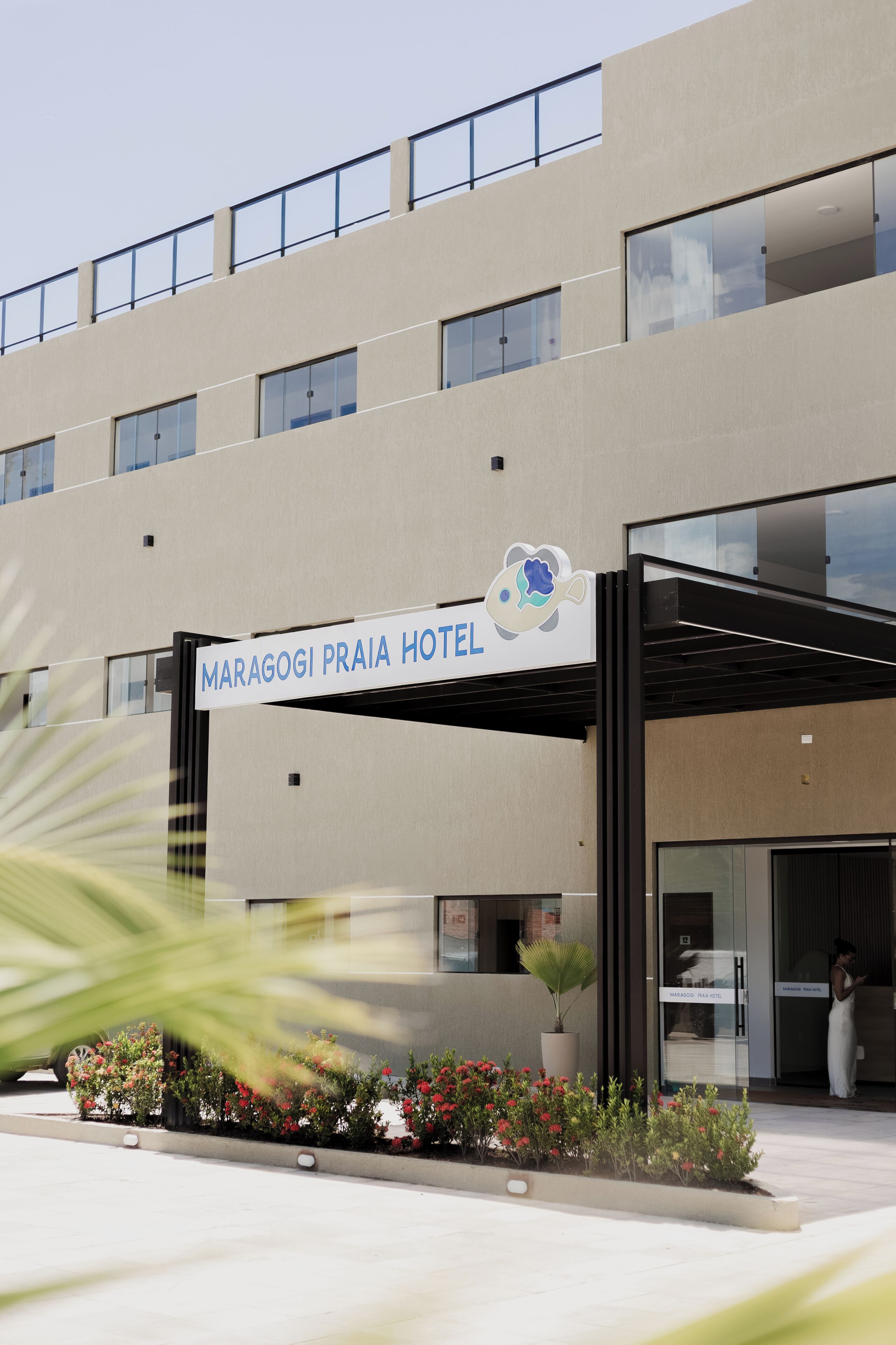 A modern building with a sign reading 'MARAGOGI PRAIA HOTEL' and a logo of a fish.