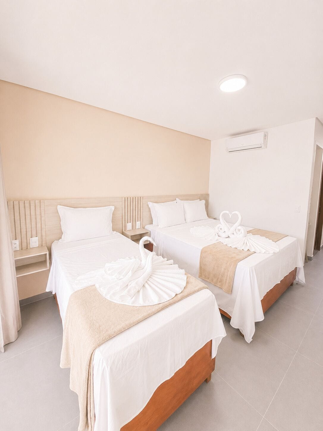 A hotel room with two beds, a bedside table, an air conditioning unit, and a door.