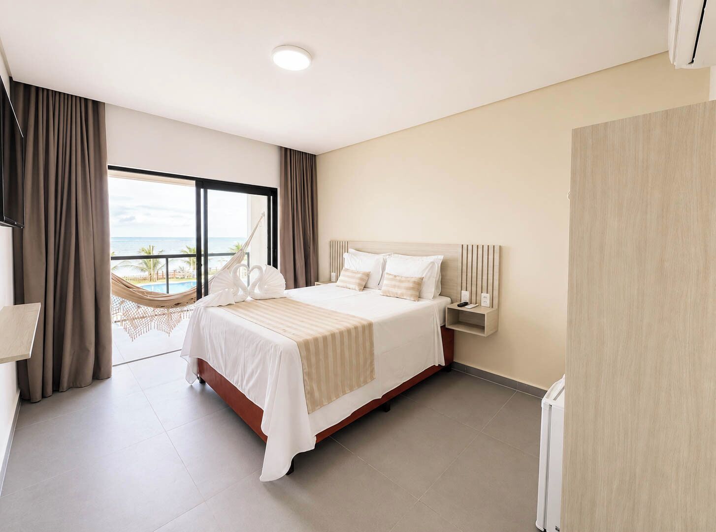 Een hotelkamer met een groot bed, een nachtkastje, uitzicht op de oceaan en een hangmat.