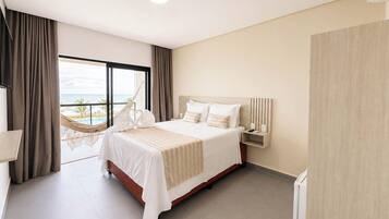 Een hotelkamer met een groot bed, een nachtkastje, uitzicht op de oceaan en een hangmat.