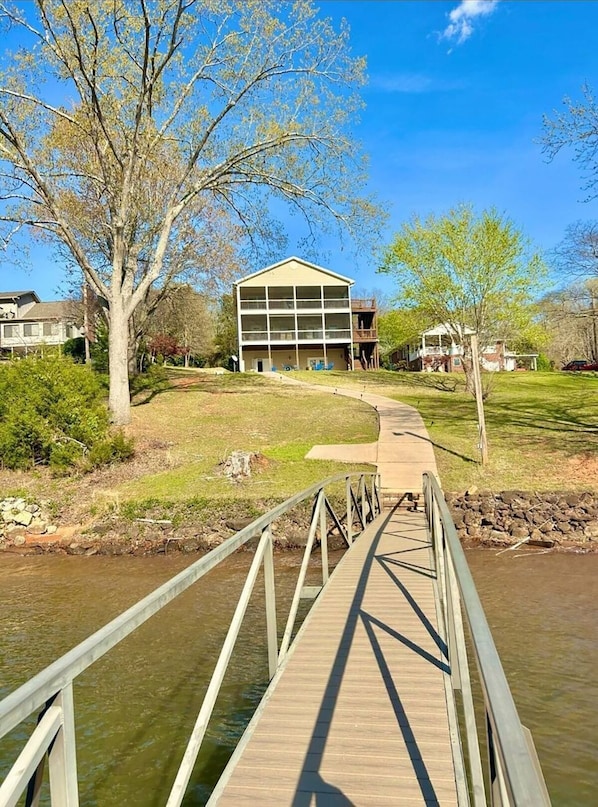A wooden bridge leading to a building with a balcony, surrounded by trees and a grassy area. - Lake Hartwell Escape w/ Dock, Games & Grill (Anderson)
