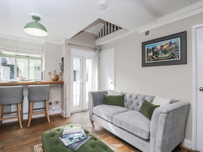 Un salon avec un canapé gris, des coussins verts, un coin repas comprenant deux chaises, une table en bois et un tableau accroché au mur.