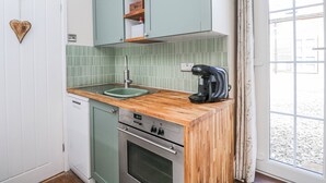 A compact kitchen with a wooden countertop, a built-in oven, and a coffee maker. - Firefly Cottage (Cirencester)