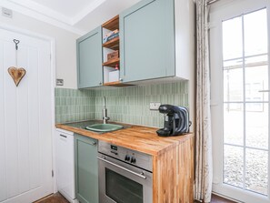 A compact kitchen with a wooden countertop, a built-in oven, and a coffee maker. - Firefly Cottage (Cirencester)