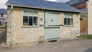 A stone cottage with a green door, numbered 12, and a small window with a basket inside. - Firefly Cottage (Cirencester)