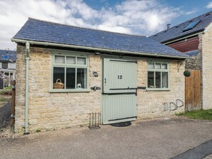 A stone cottage with a green door, numbered 12, and a small window with a basket inside. - Firefly Cottage (Cirencester)