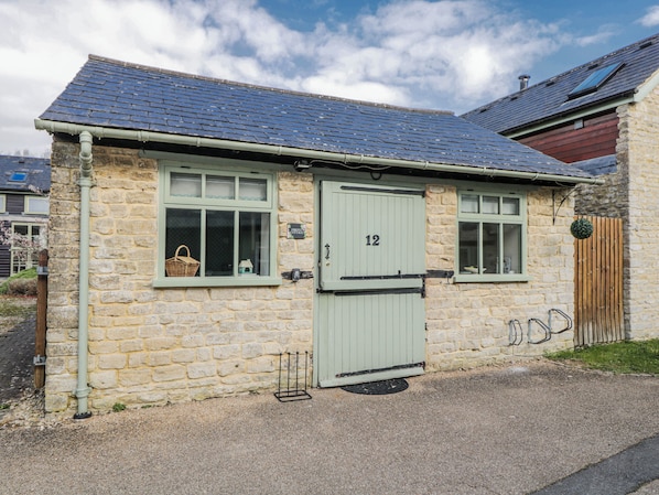 A stone cottage with a green door, numbered 12, and a small window with a basket inside. - Firefly Cottage (Cirencester)