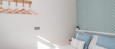 Un dormitorio con una cama, un aplique de pared, un perchero de madera y una pared con estampado.