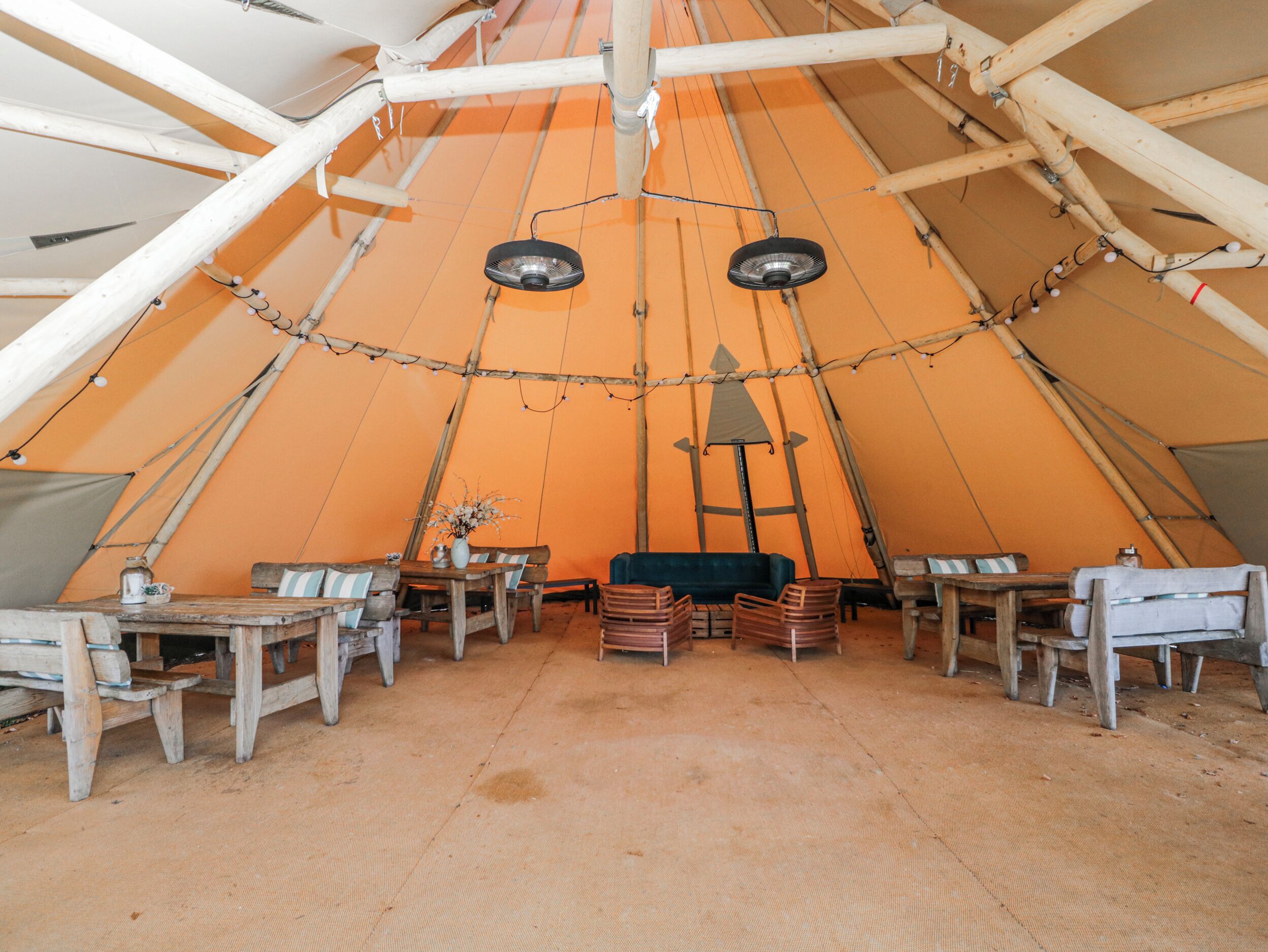 A large tent with a high ceiling, wooden furniture, and a central table with chairs.
