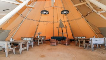 A large tent with a high ceiling, wooden furniture, and a central table with chairs.