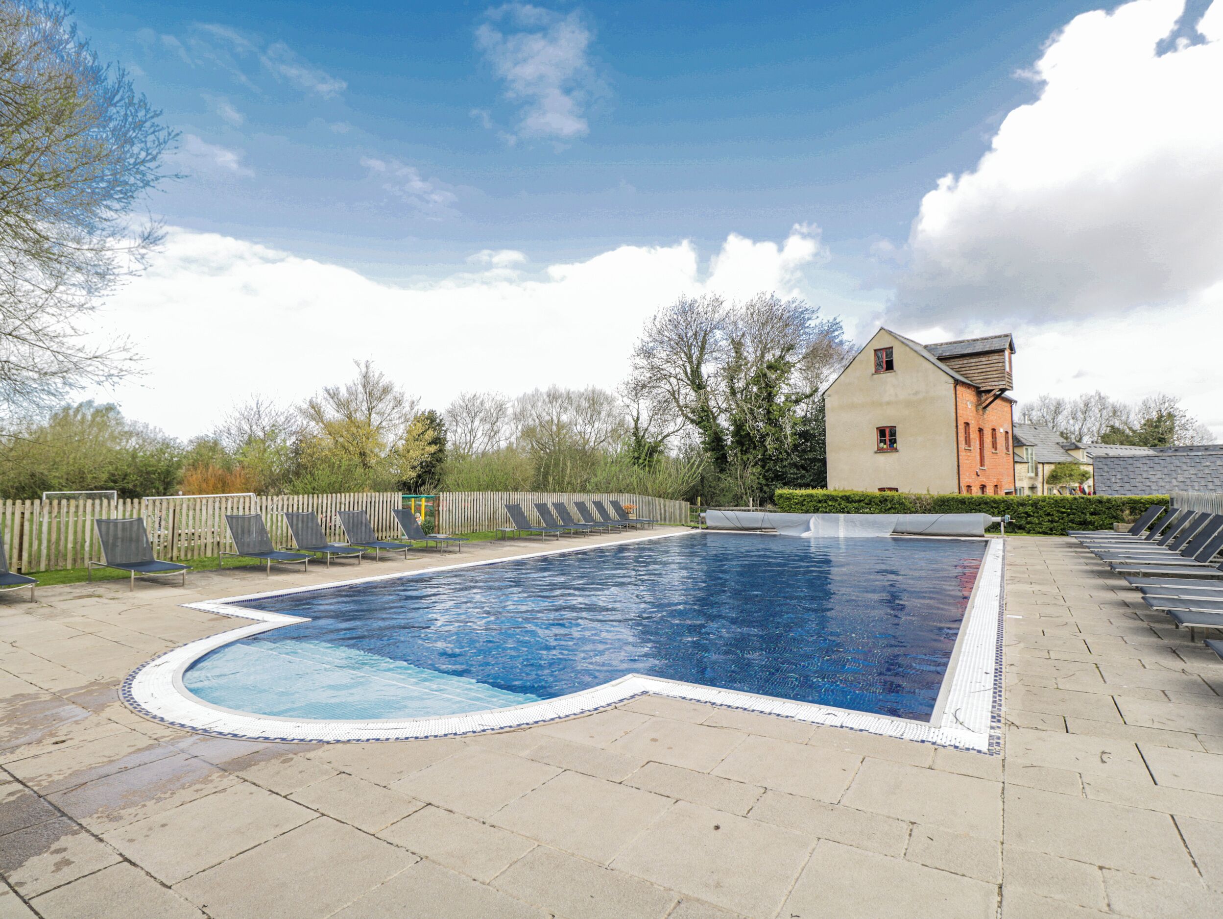 A swimming pool with a wooden deck, lounge chairs, and a building in the background.