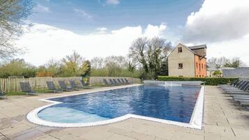A swimming pool with a wooden deck, lounge chairs, and a building in the background.