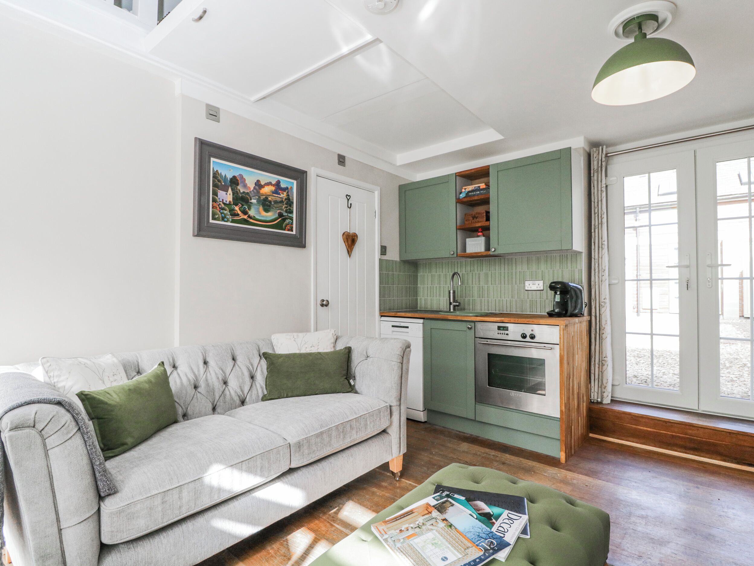 A modern kitchen with a built-in oven, a dining area with a green table, and a grey sofa with green cushions.