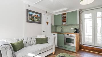 A modern kitchen with a built-in oven, a dining area with a green table, and a grey sofa with green cushions.
