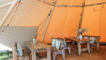 A tent with a table and benches, a vase with flowers, and a bottle on the table.