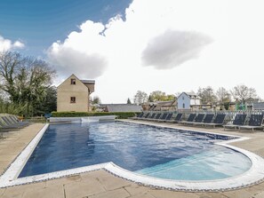 Una piscina con borde de azulejos, rodeada por una valla y edificios al fondo.