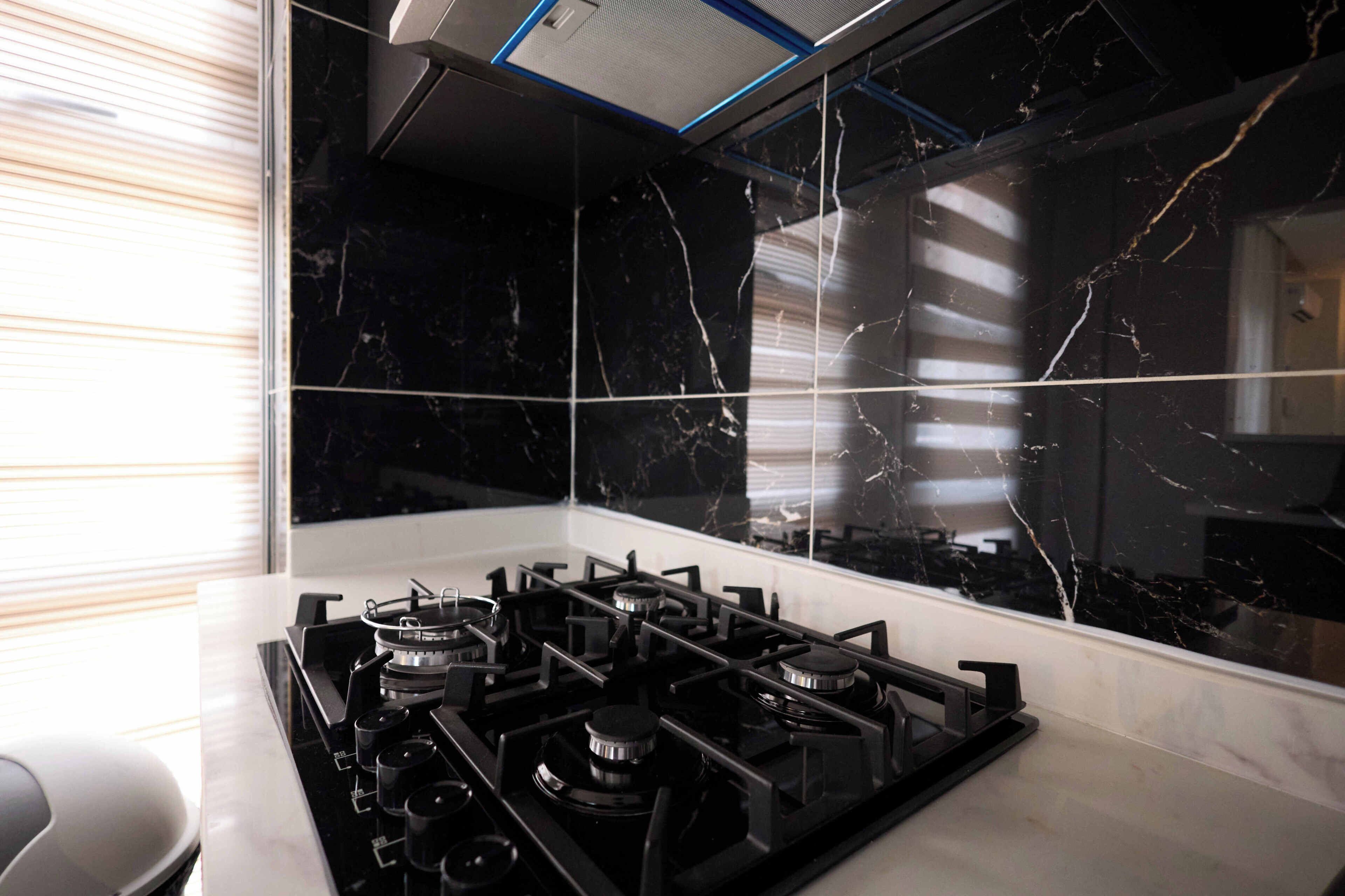 A kitchen with a gas stove, black marble backsplash, and a window with blinds.