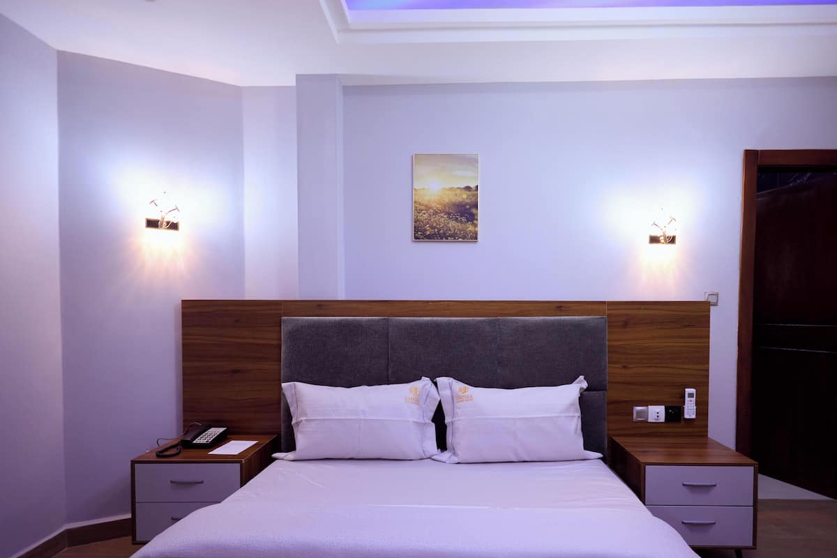 Habitación de hotel con cama, mesitas de noche, teléfono y un cuadro en la pared.