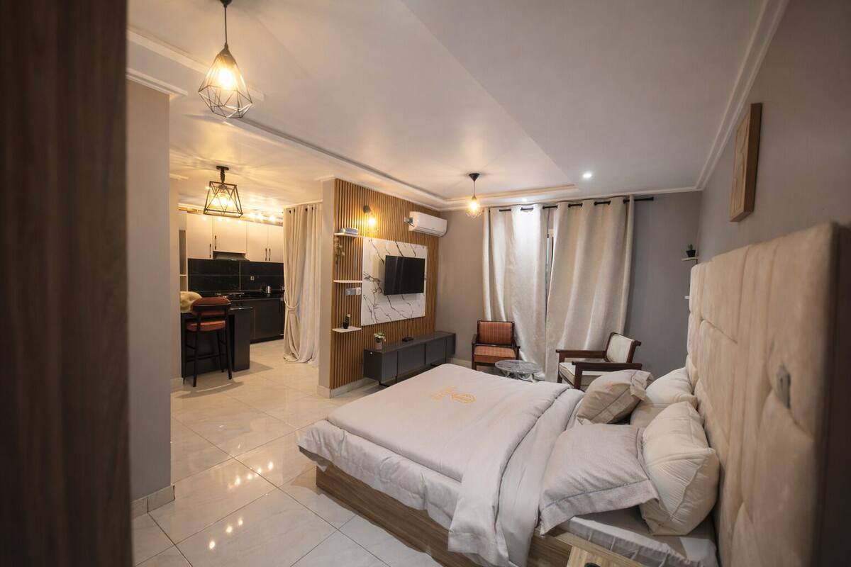 Un dormitorio moderno con una cama grande, un televisor montado en la pared y una zona de comedor independiente.