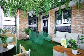 A cozy outdoor seating area with a brick wall, green chairs, a white sofa, and a small table. - EMPIRE LUXURY HOTEL (Yaoundé)