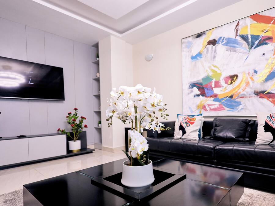 A modern living room with a flat-screen TV, a black leather sofa, a coffee table, and a large abstract painting.