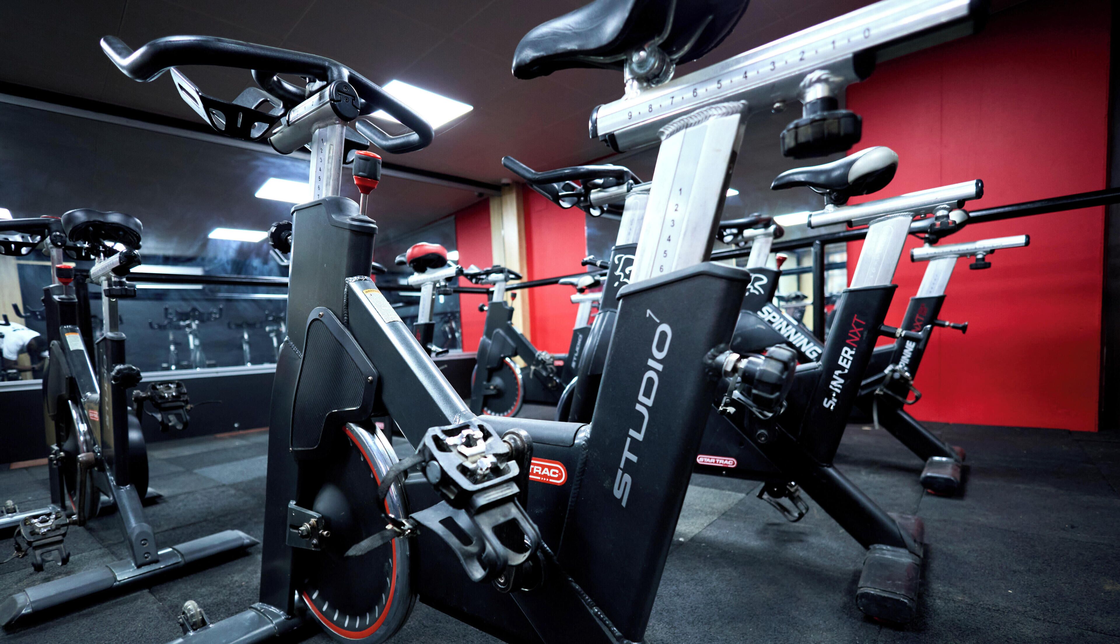 Una palestra con cyclette, macchinari per pesi e un muro rosso.
