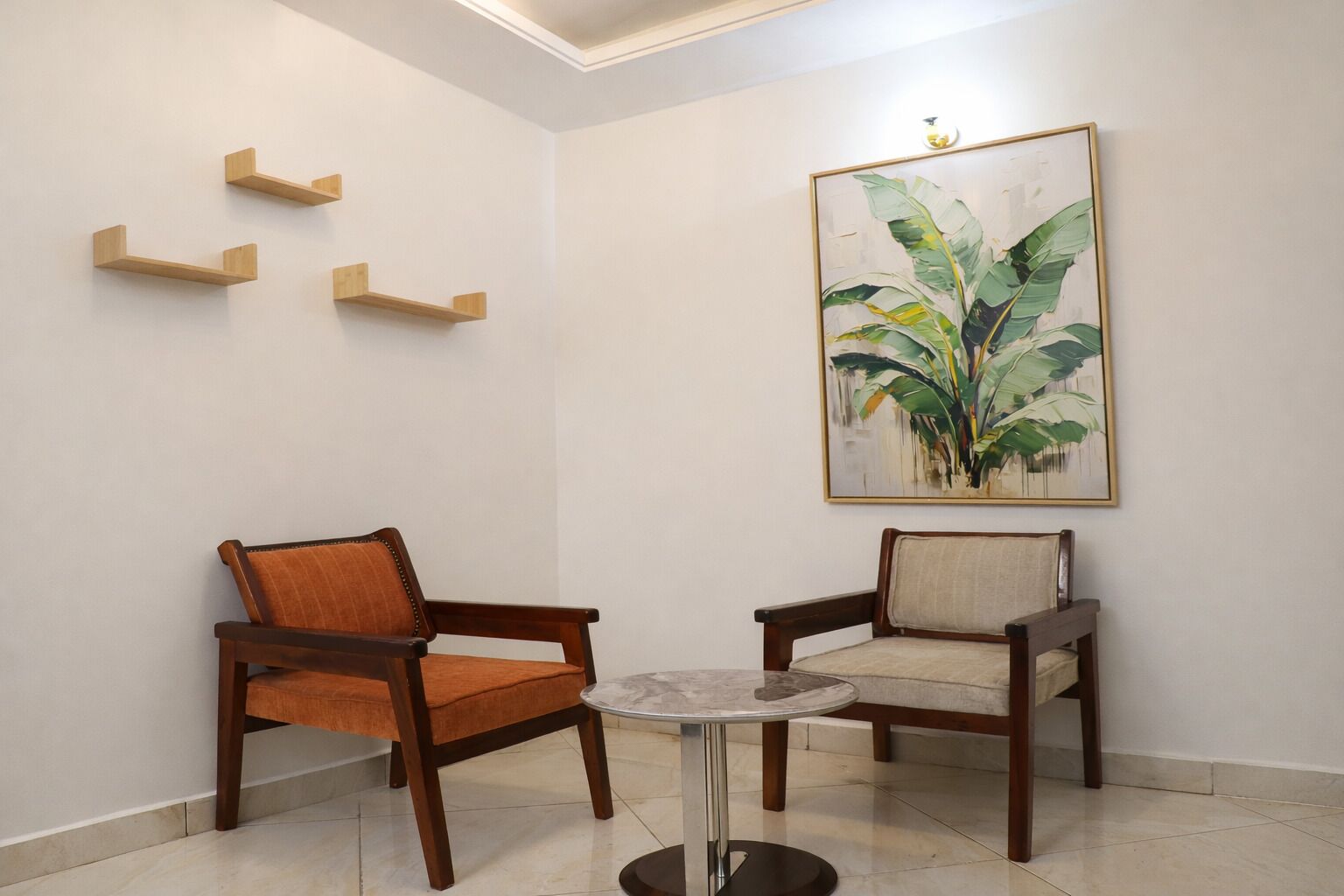 A room with two wooden chairs, a small round table, and a large framed botanical painting on the wall.