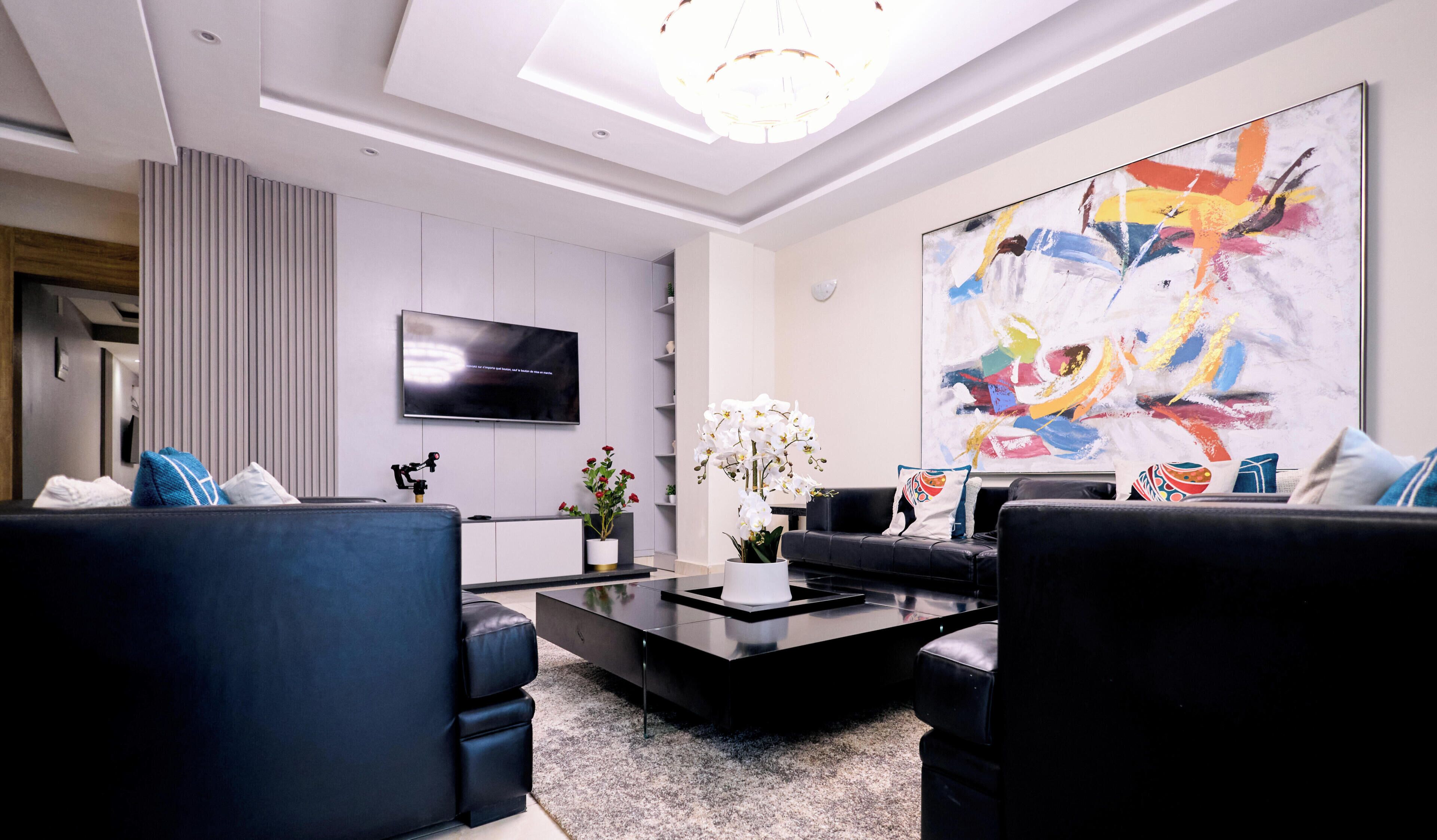 A modern living room with a flat-screen TV, a coffee table, two sofas, and a large abstract painting.