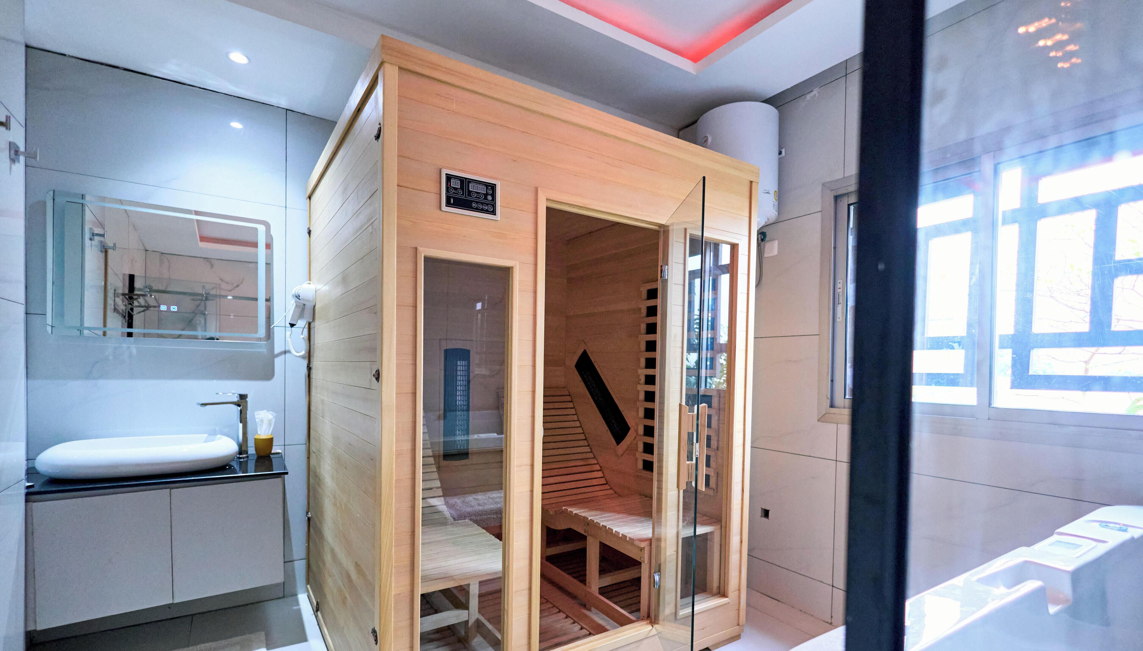 A modern bathroom with a wooden sauna, a sink, and a glass shower enclosure.