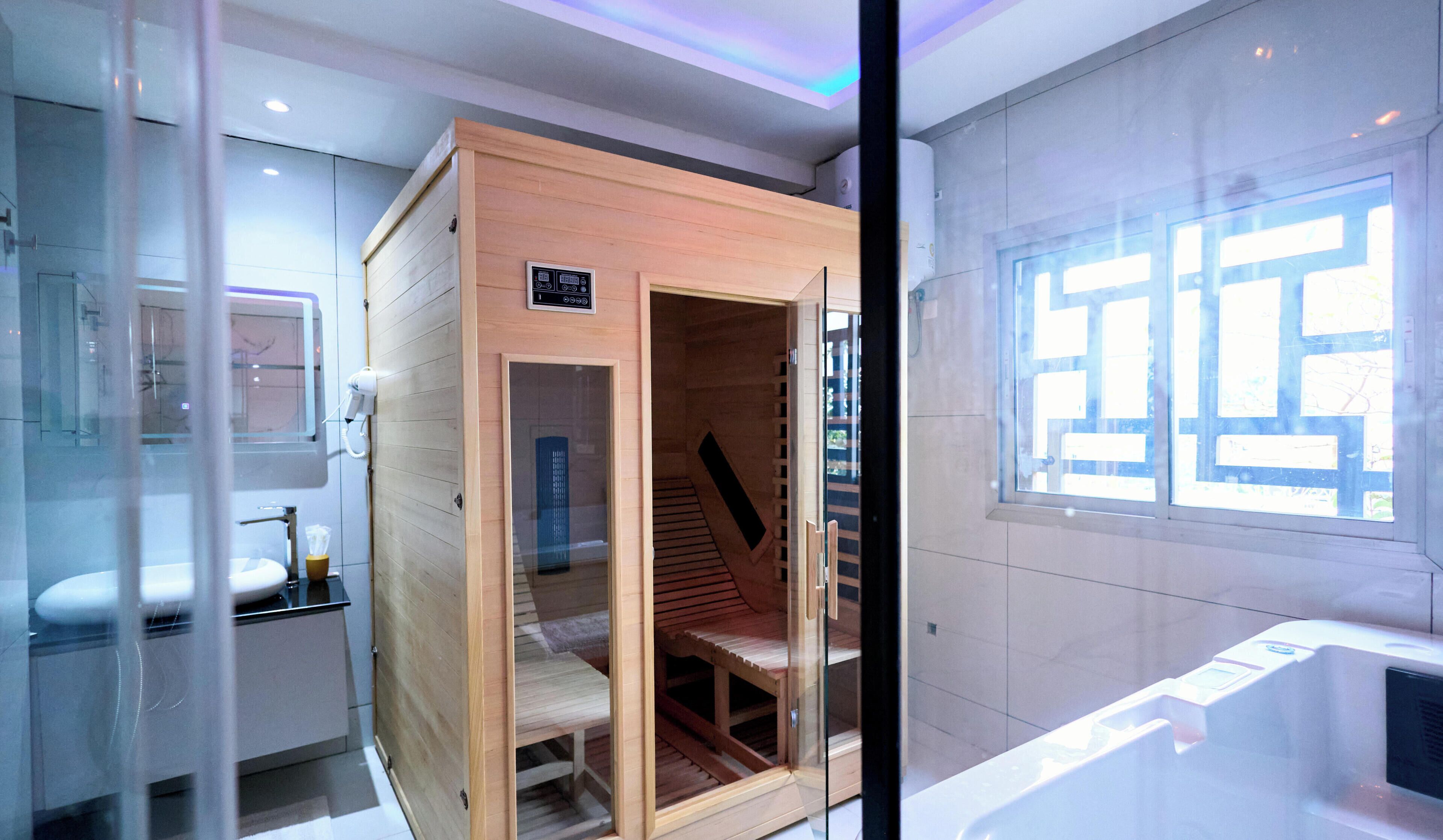 A modern bathroom with a glass shower enclosure, a wooden sauna, and a large window with a geometric view.