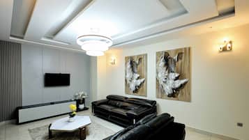 A modern living room with a black leather sofa, a white coffee table, a flat-screen TV, and two abstract paintings on the wall.