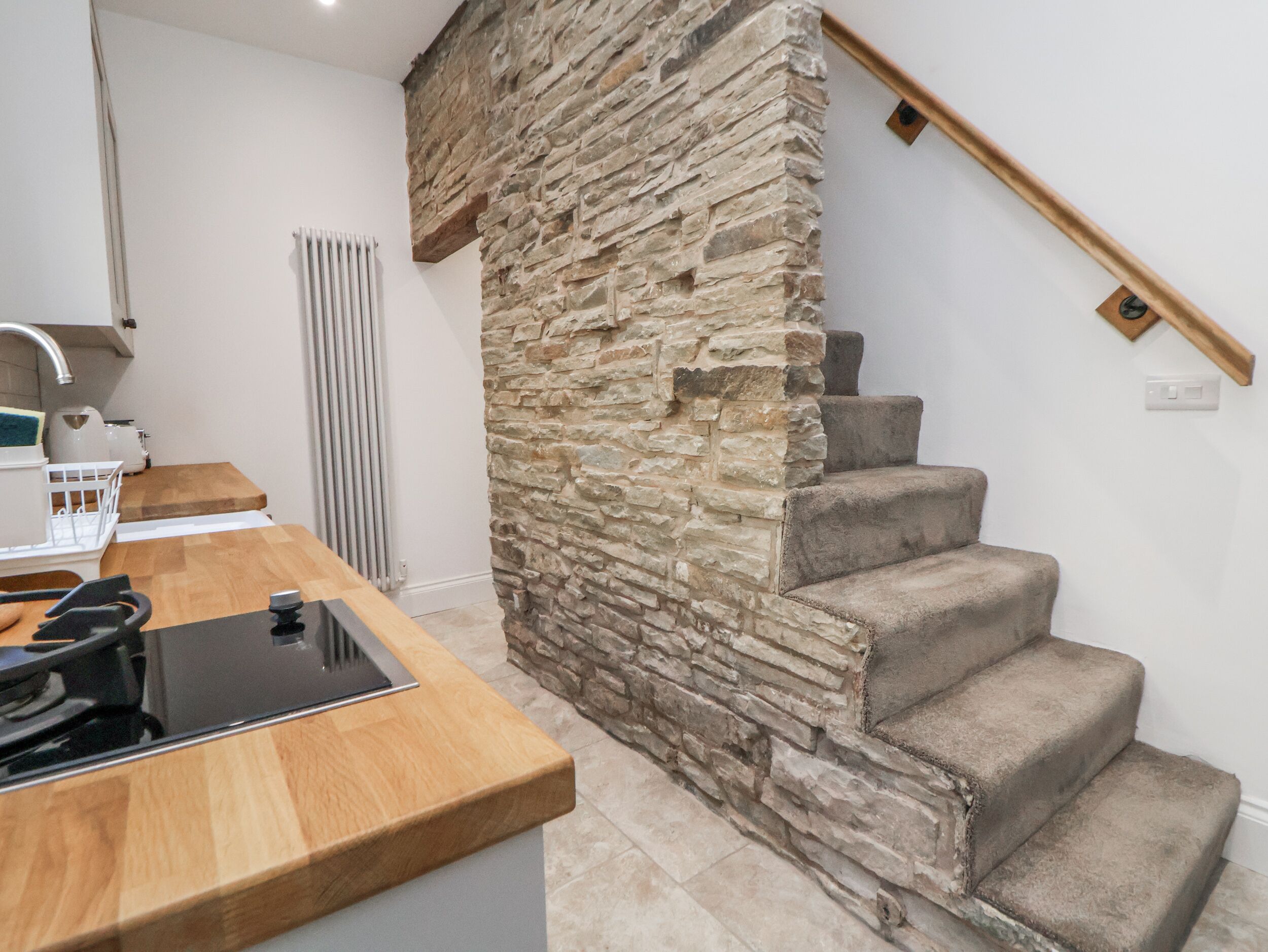 Una cocina con un muro de acento de piedra, encimera de madera y una escalera con barandilla de madera.