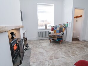 A living room with a fireplace, a radiator, a window with blinds, a colorful armchair, and a red cushion. - 10 South Street (Rossendale)