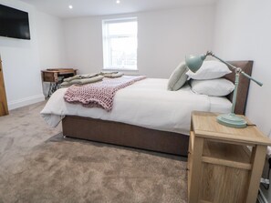A bedroom with a bed, a bedside lamp, a window, a TV, and a desk. - 10 South Street (Rossendale)