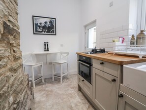 A kitchen with white cabinets, a wooden countertop, a stove, and a sink. There is a framed picture on the wall and a window above the sink. - 10 South Street (Rossendale)