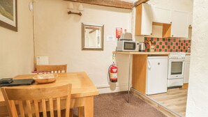 A compact kitchen with a wooden table, a microwave, a small oven, and a fire extinguisher. - Mews Cottage 5 (Keswick)