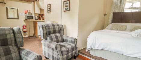 A room with a bed, two plaid armchairs, a kitchenette, and a fire extinguisher.