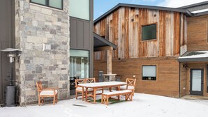 A modern building with a stone facade and wooden exterior, a patio with a table and chairs, and a snow-covered ground. - Base Camp Townhome #106 Slopeside 3 bedroom townhome, views, private balcony (Granby)