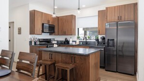 A modern kitchen with wooden cabinets, stainless steel appliances, and a central island with bar stools. - Base Camp Townhome #106 Slopeside 3 bedroom townhome, views, private balcony (Granby)