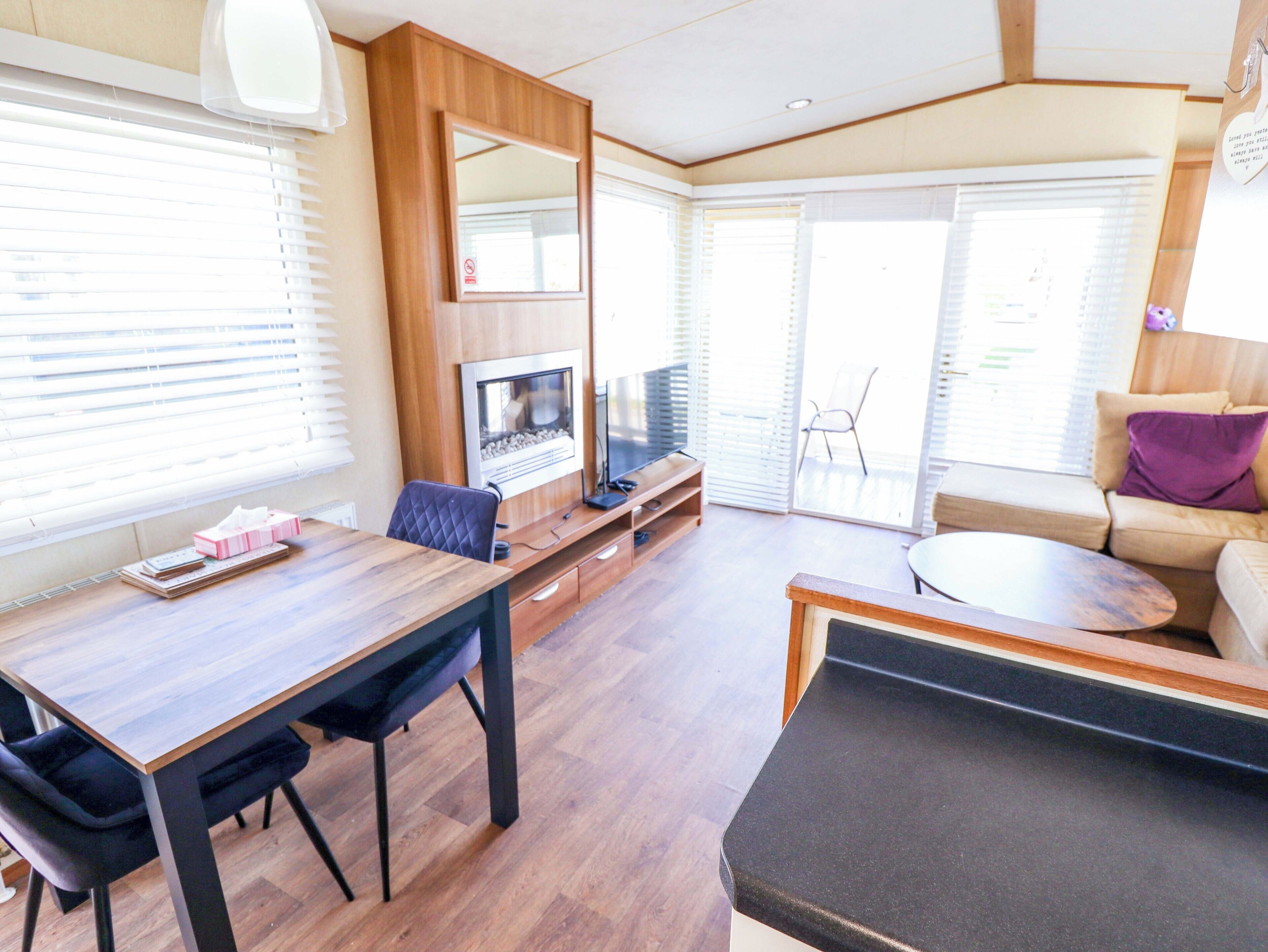 A modern living room with a wooden dining table, a sofa, a TV, and a fireplace.