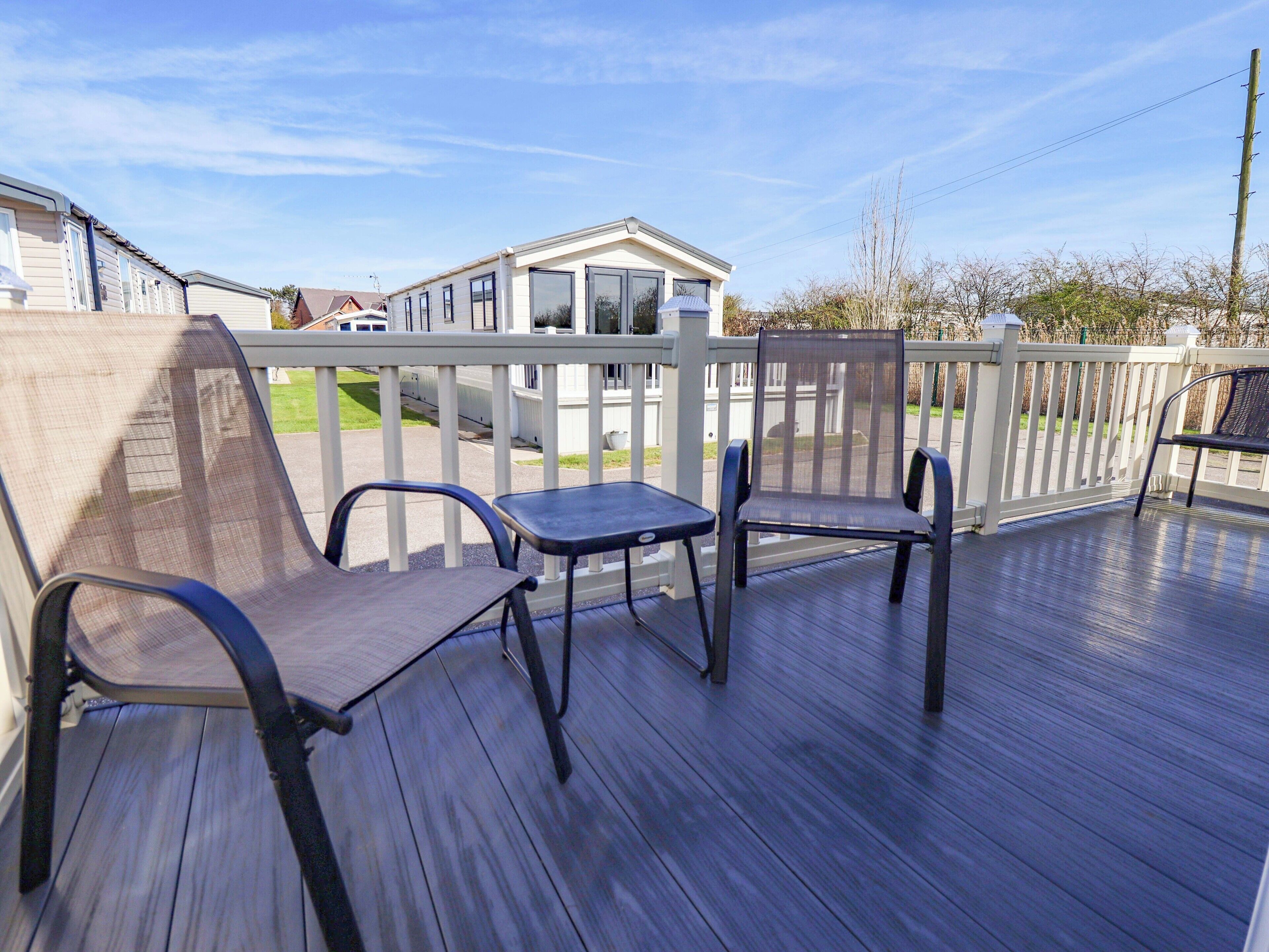 Eine Terrasse mit drei Stühlen, einem Tisch, einem weißen Geländer und einem Haus im Hintergrund.