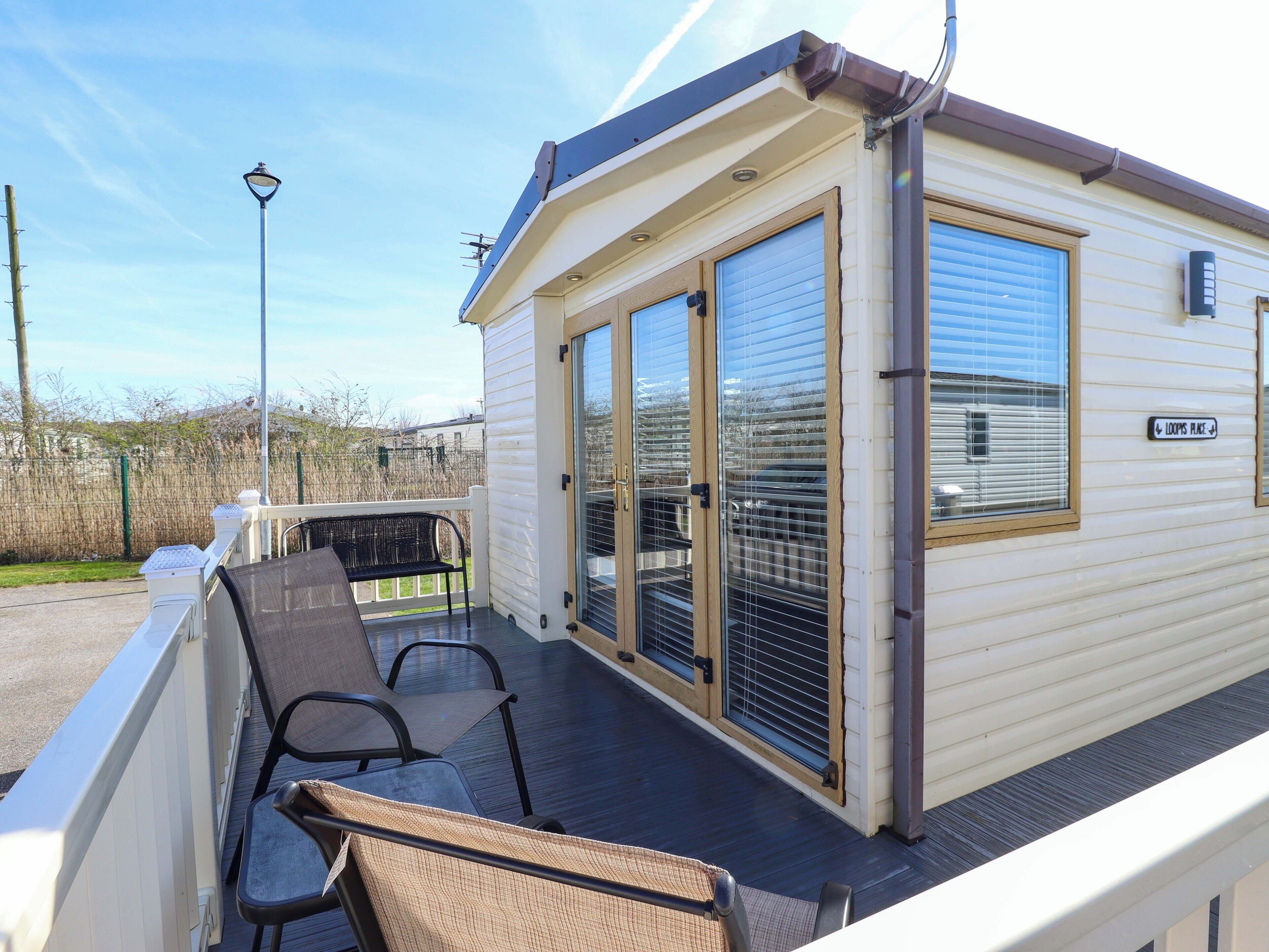 A small, single-story mobile home with a covered deck, two sliding glass doors, and a sign reading 'LOOPS PLACE'.