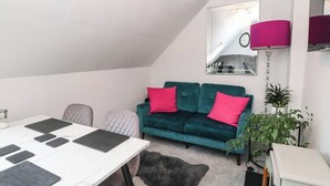 A modern living room with a white ceiling, a teal sofa with pink cushions, a white table with black placemats, a gray furry rug, and a mirror on the wall. - 3 Linshader (Isle of Lewis)