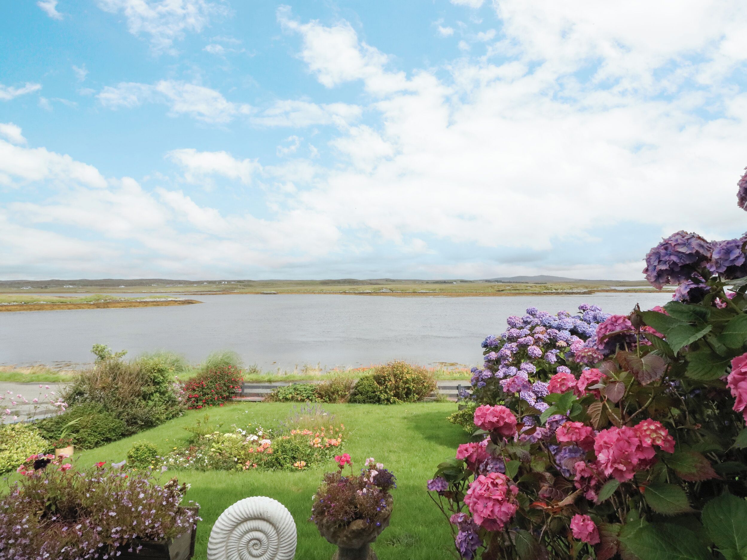 A landscaped garden with a variety of flowers and a spiral stone sculpture.