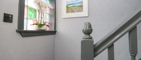 A staircase with a handrail, a wall-mounted light switch, a window with a plant, and a framed picture.