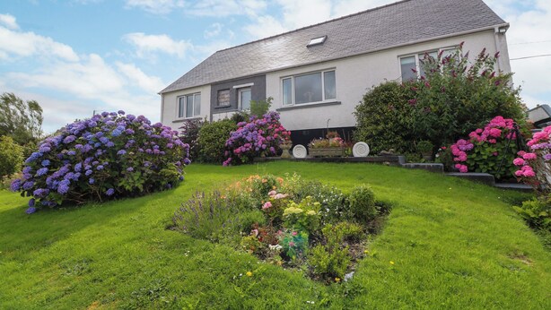 A two-story house with a sloped roof, surrounded by a well-maintained garden with various flowering plants. - 3 Linshader (Isle of Lewis)
