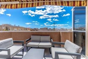 A rooftop terrace with a view of the city, a striped awning, and a seating area with cushions. - Penthouse in Central Torrevieja (Torrevieja)